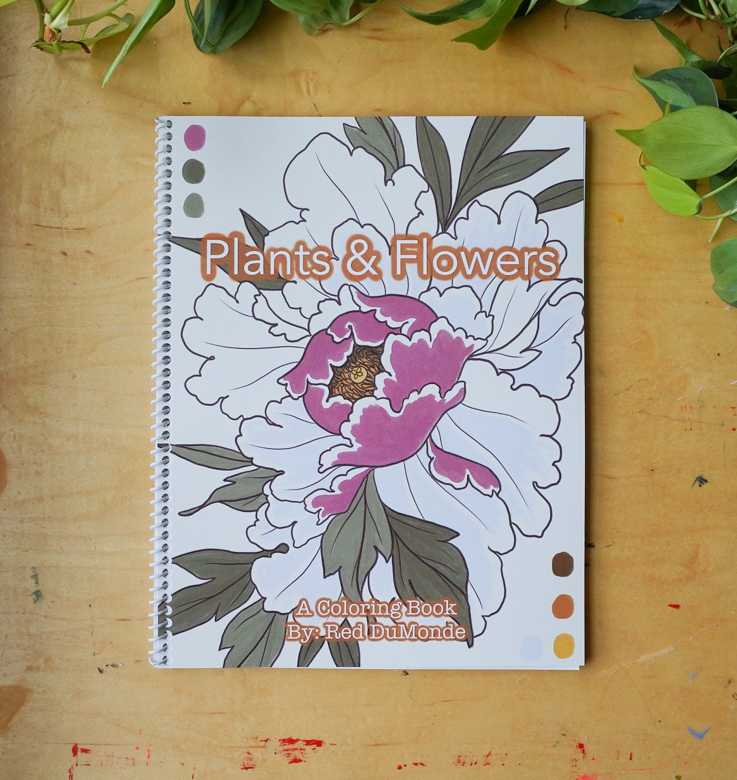 Spiral bound coloring book laying flat on a wood table with some leaves at the top of the image