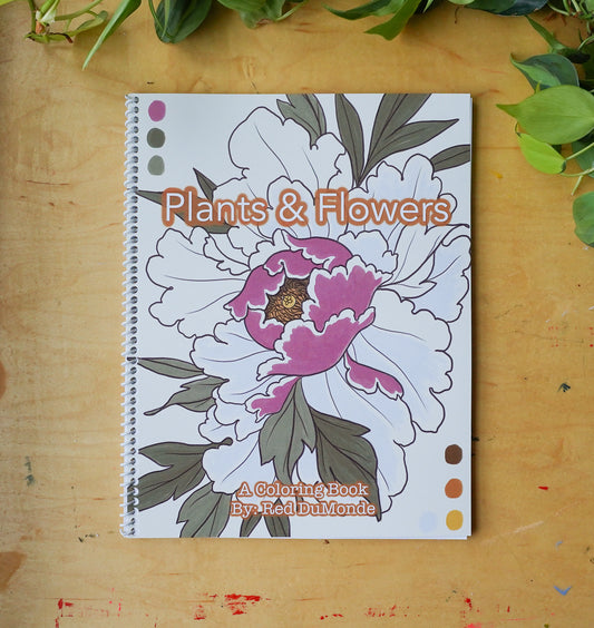 Spiral bound coloring book laying flat on a wood table with some leaves at the top of the image