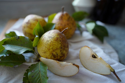 Pear still life blog. An image of pears with leaves and some cut slices on a white towel in a kitchen.