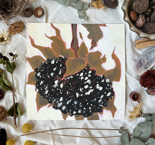 Art print of a large dried sunflower head with an off white background. Print is sitting on a white linen sheet surrounded by dried plants and other nature items.