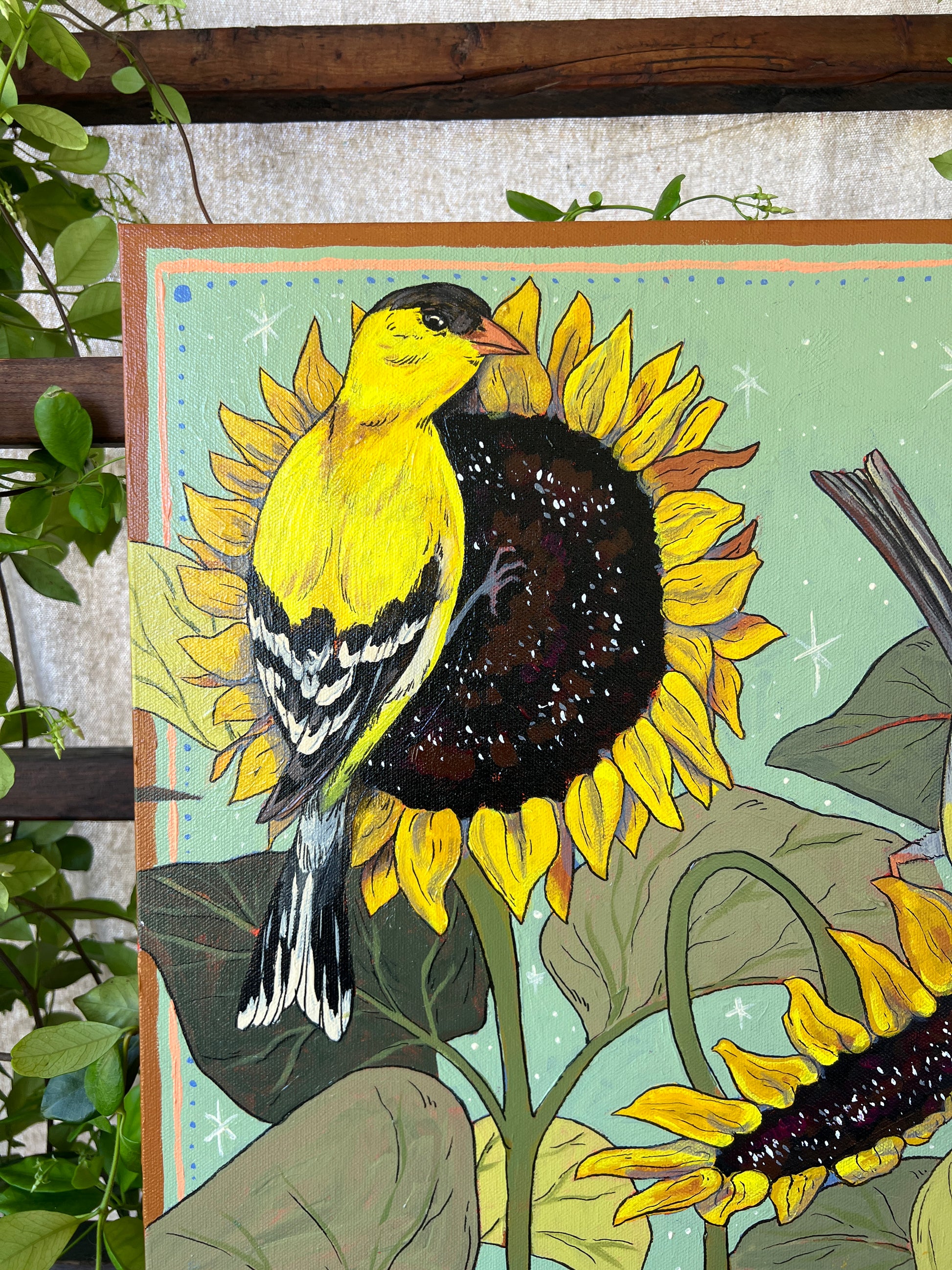 Detail of original painting with male gold finch on sunflowers, surrounded by greenery
