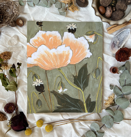 Art print of peachy pink poppy and buds and seed pods on a green/grey background. Print is sitting on a white linen sheet surrounded by dried plants and other nature items.