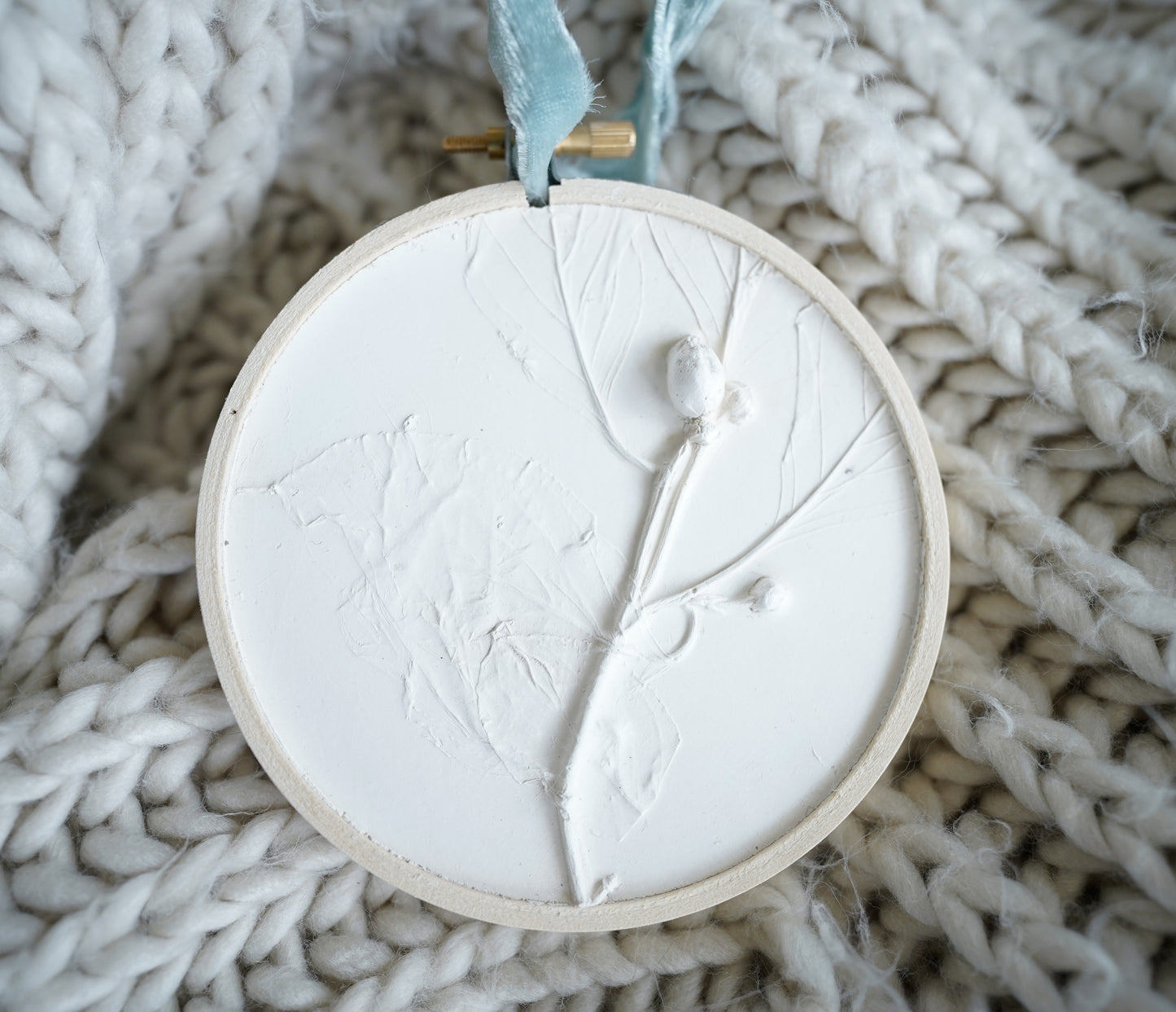 plaster cast of a dogwood branch in a round wooden embroidery hoop frame with a light blue velvet ribbon